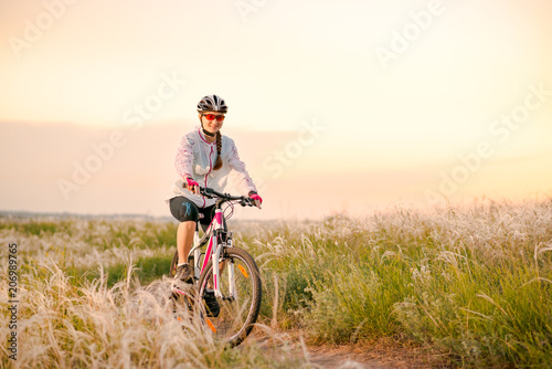 Young Woman Riding Mountain Bikes in the Beautiful Field of Feather Grass at Sunset. Adventure and Travel.
