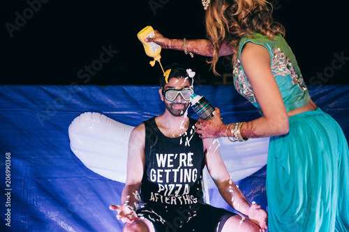 People cover Hindu groom with different sauces on a pre-wedding party photo