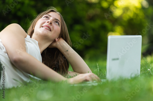 Young dark blonde girl studying in a park with a laptop