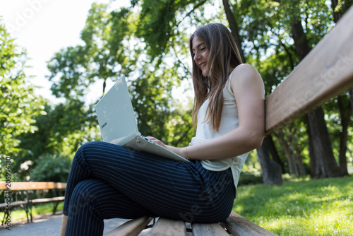Young dark blonde girl studying in a park with a laptop