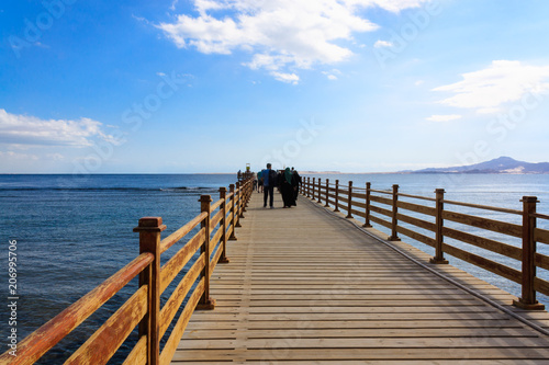 People walking along a long pier to the sea. Bridge. In the background, mountains. Egypt. Relax in summer and winter. The concept of rest and relax. Vacation. 
