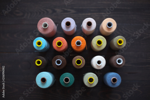 Rows of colourful bobbins with coloured threads on a wooden background