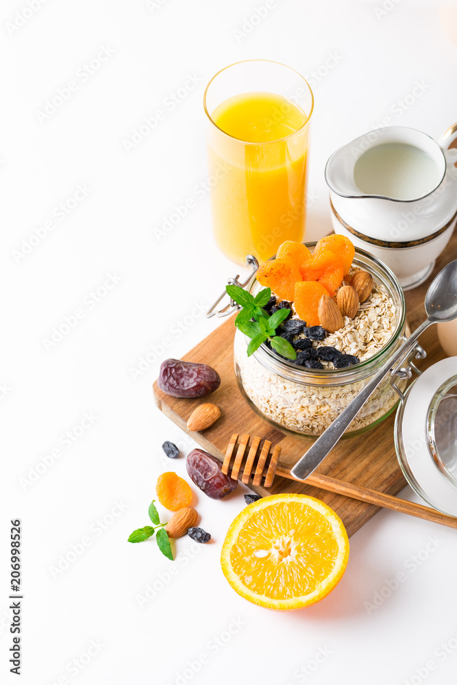 Healthy breakfast in glass mason jar with oat flakes, granola, milk, dry fruits and nuts, dates, honey, orange juice, eggs for morning fitness on wooden board platter on white background isolated Healthy breakfast in glass mason jar with oat flakes, granola, milk, dry fruits and nuts, dates, honey, orange juice, eggs for morning fitness on wooden board platter on white background isolated