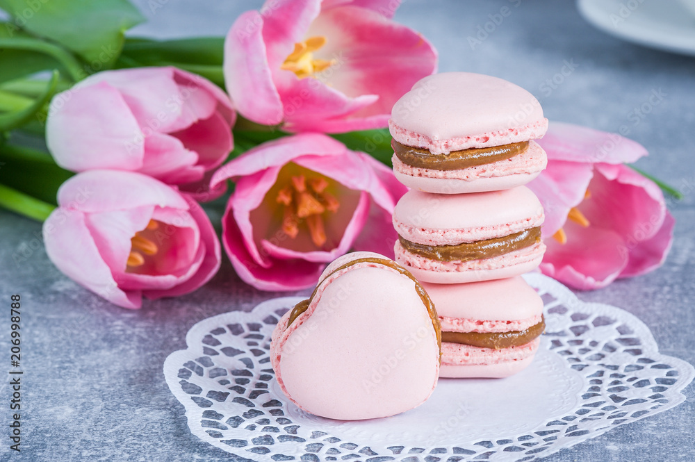 Strawberry macarons with pink tulips  on blue texture background. Heart shaped. French delicate dessert. Copy space, selective focus. Spring concept.