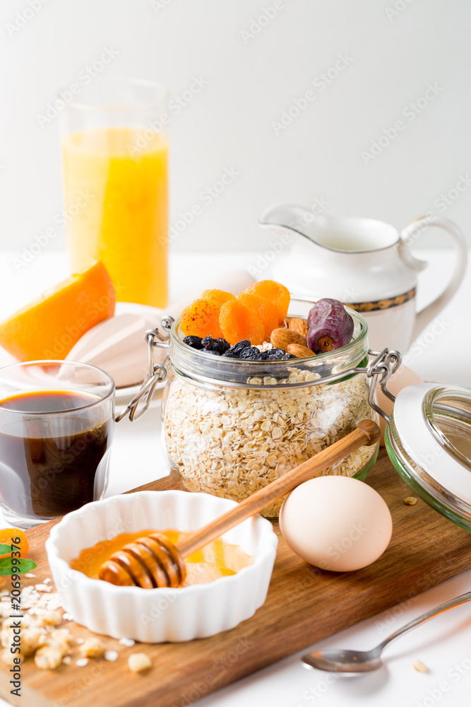Healthy breakfast in glass mason jar with oat flakes, granola, milk, dry fruits and nuts, dates, honey, orange juice, eggs for morning fitness on wooden board platter on white background isolated Healthy breakfast in glass mason jar with oat flakes, granola, milk, dry fruits and nuts, dates, honey, orange juice, eggs for morning fitness on wooden board platter on white background isolated