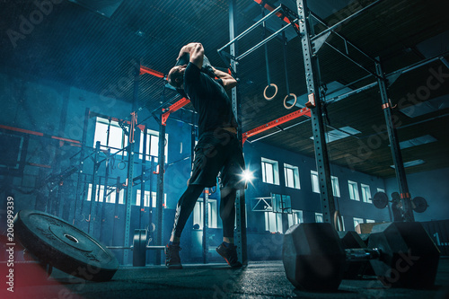 Foto Fit young man lifting barbells working out in a gym