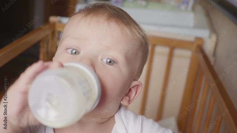 Two year old boy drinking milk from plastic bottle in his bed looking up Two year old boy drinking milk from plastic bottle in his bed looking up