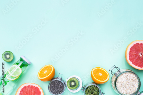 Food for fitness, healthy lifestyle frame flat lay with fresh fat burning fruits orange and grapefruits slices, complex carbohydrates, detox water bottle, pink hand weights, light green background