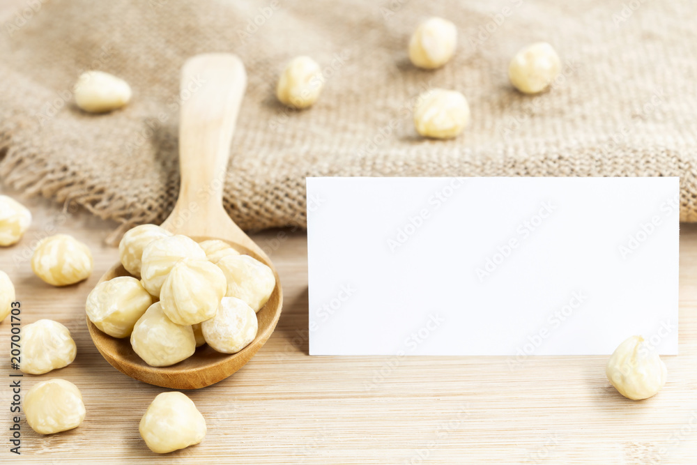 Hazelnuts nut peeled with wooden spoon and paper white mock up on the wood table background. Creative layout with nature concept with space for text.