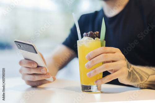 Attractive young man is holding mobile phone and drinking lemonade.