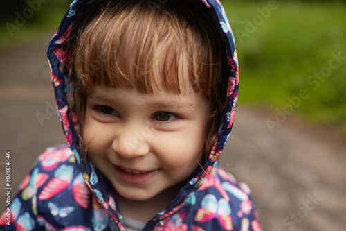Funny little girl in rain coat stands in green park