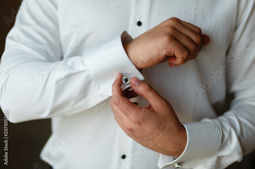 Close-up hands of man buttons cuff link on French cuffs sleeves luxury white shirt. The groom is preparing for the wedding, going to meet with the bride. Hands of wedding groom getting ready in suit