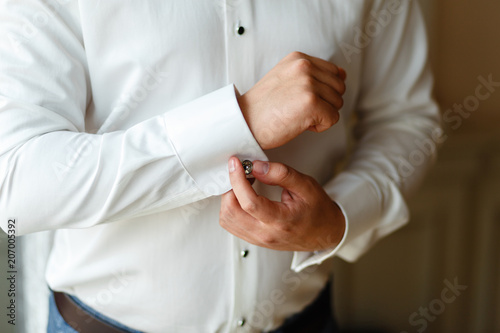 Close-up hands of man buttons cuff link on French cuffs sleeves luxury white shirt. The groom is preparing for the wedding, going to meet with the bride. Hands of wedding groom getting ready in suit
