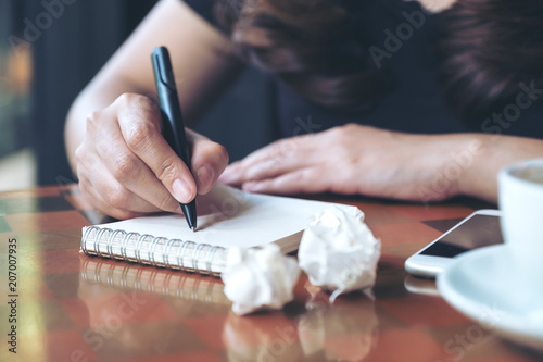Closeup image of a businesswoman working and writing down on a white blank notebook with screwed up papers on table