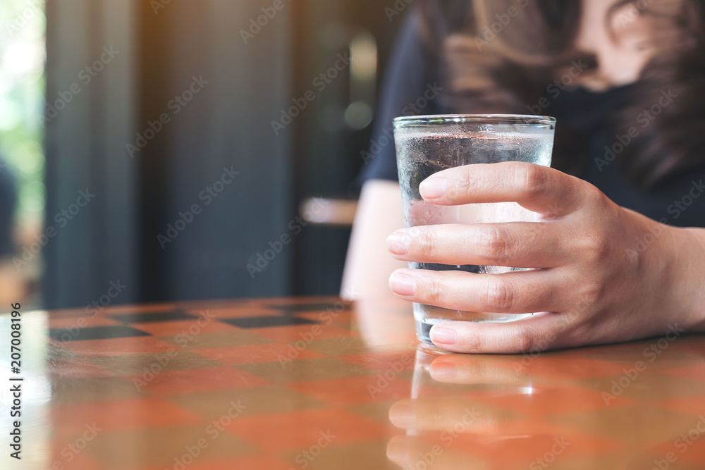 Closeup image of woman's hand holding a glass of cold water on table Closeup image of woman's hand holding a glass of cold water on table