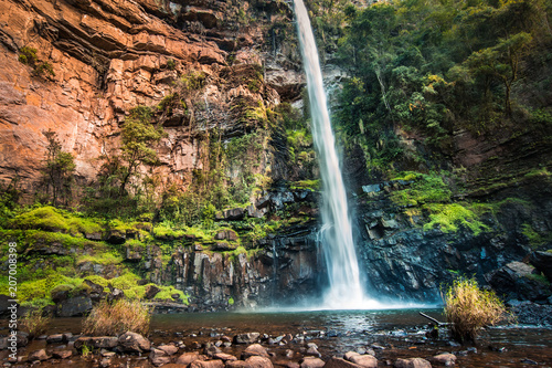 Wide view of Lone Creek Falls South Africa  a tall thin waterfall with red cliffs and vibrant greenery