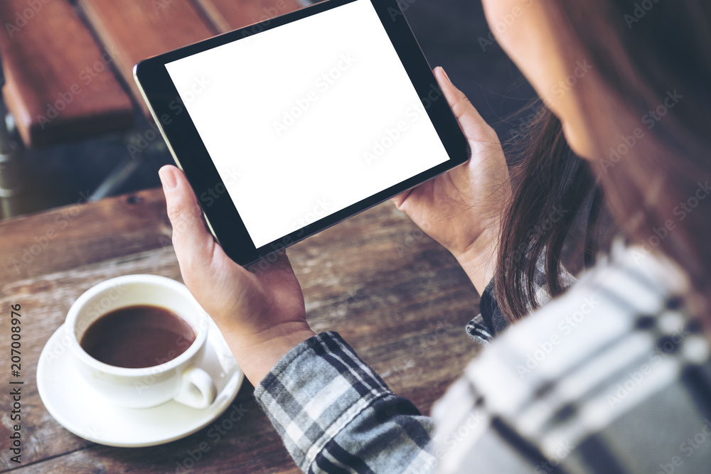 Mockup image of a woman holding black tablet pc with white blank screen with coffee cup on table background Mockup image of a woman holding black tablet pc with white blank screen with coffee cup on table background