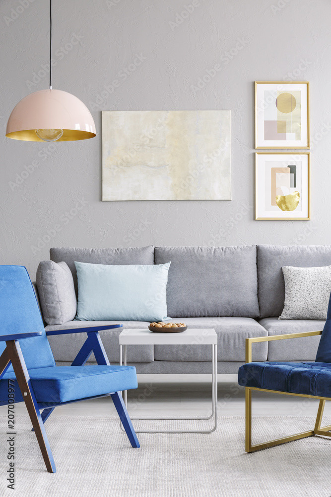 Real photo of two blue chairs standing in front of a grey couch in a ...