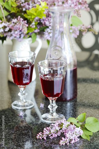 Berry drink in glass and bouquet of lilac in the table. Summer cold drink.