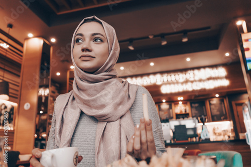 a cute Muslim girl in hijab sits in a restaurant and eats a delicious meal, smiling