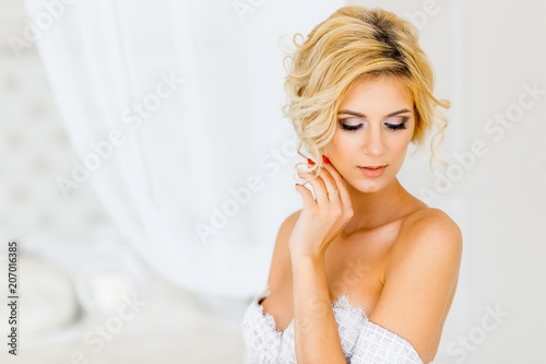 A portrait of a beautiful bride with hairstyle and make up lying on her dress. A beautiful girl with blond hair and blue eyes smiling
