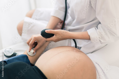 Female Obstetrician doctor  measuring blood pressure of the pregnant woman in the hospital. Pregnancy-induced Hypertension concept.