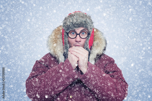 Frozen man in winter clothes warming hands, cold, snow, blizzard 