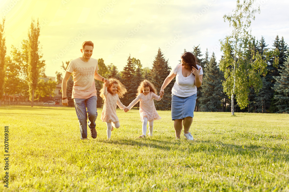Fototapeta premium Smiling Family Running Across Summer Field Together, happy family with twin toddler girls