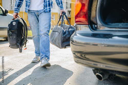 young adult man putting bag in car trunk. car travel concept