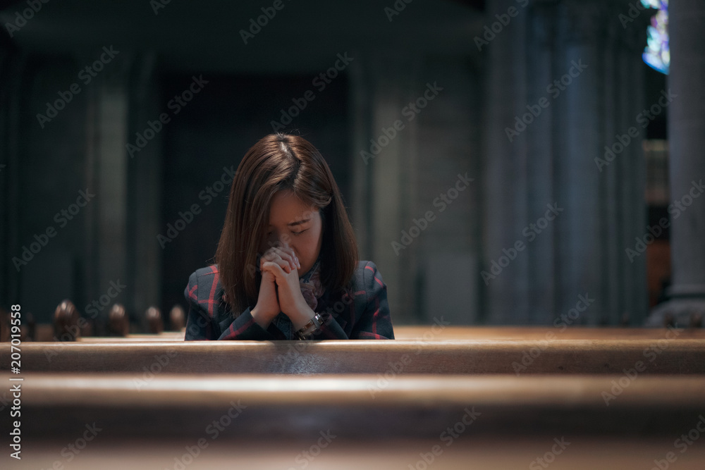 Fototapeta premium A Christian girl is sitting and praying with broken heart in the church.