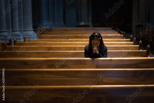 A Christian girl is sitting and praying with broken heart in the church.
