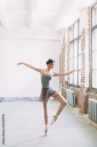 Fototapeta Naklejka Na Ścianę i Meble -  A young ballerina is getting ready, stretched and dancing. Poses in ballet. Photo shoot in the loft Studio. Russian Ballerina at the bench. ballet flats and dance dress