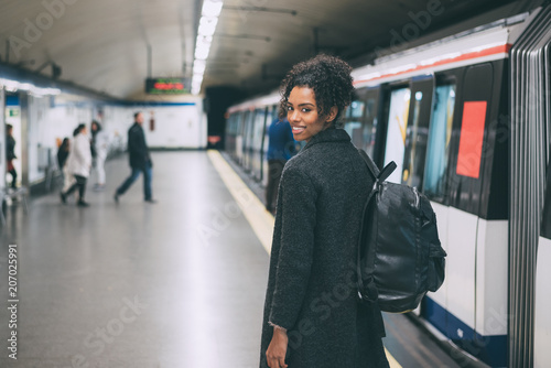 Happy young black woman inside the underground station waiting for the train