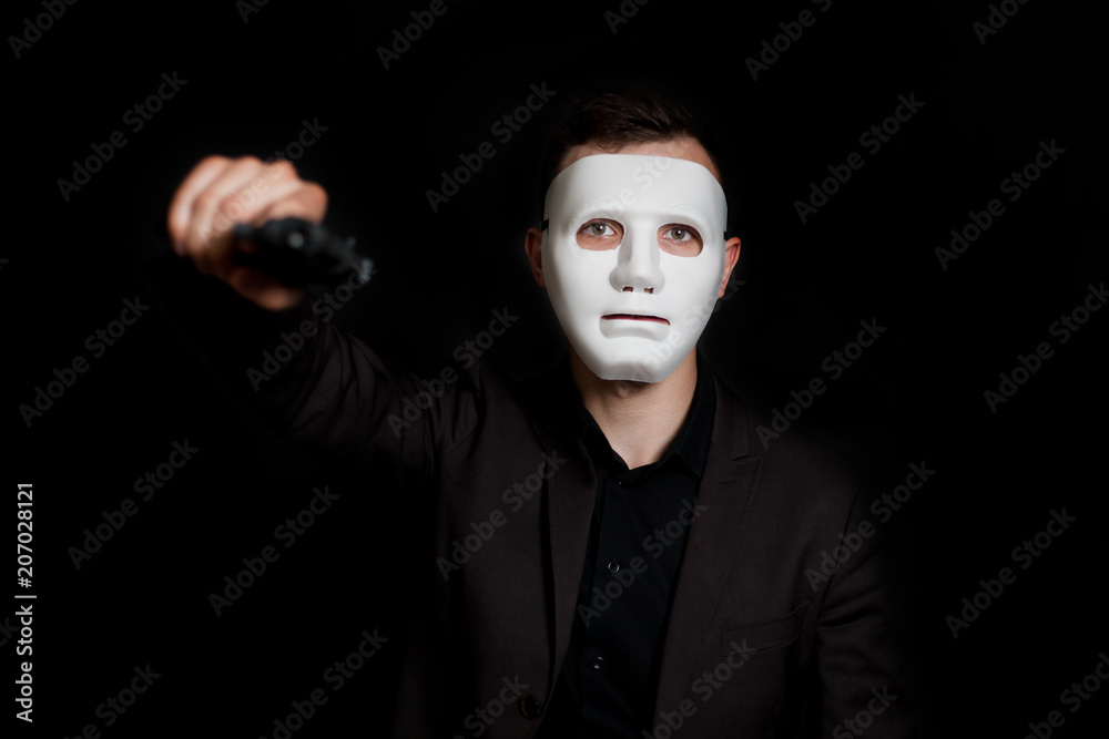 Man on a black background in a white mask. Threatens with a pistol. Man on a black background in a white mask. Threatens with a pistol.