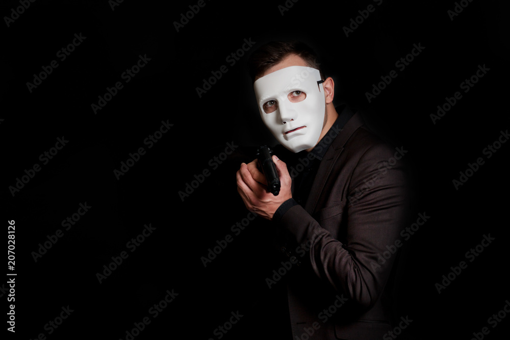 A man with a gun in his hand, in a white mask on a black Stock Photo Adobe Stock