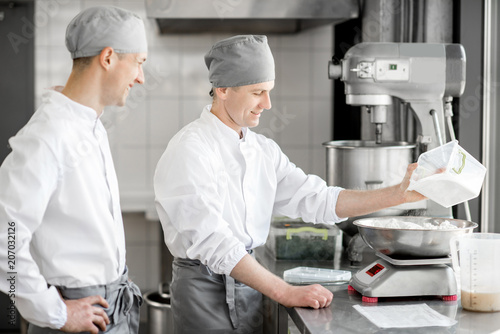 Two handsome male confectioners in uniform weighing ingredients for baking at the manufacturing