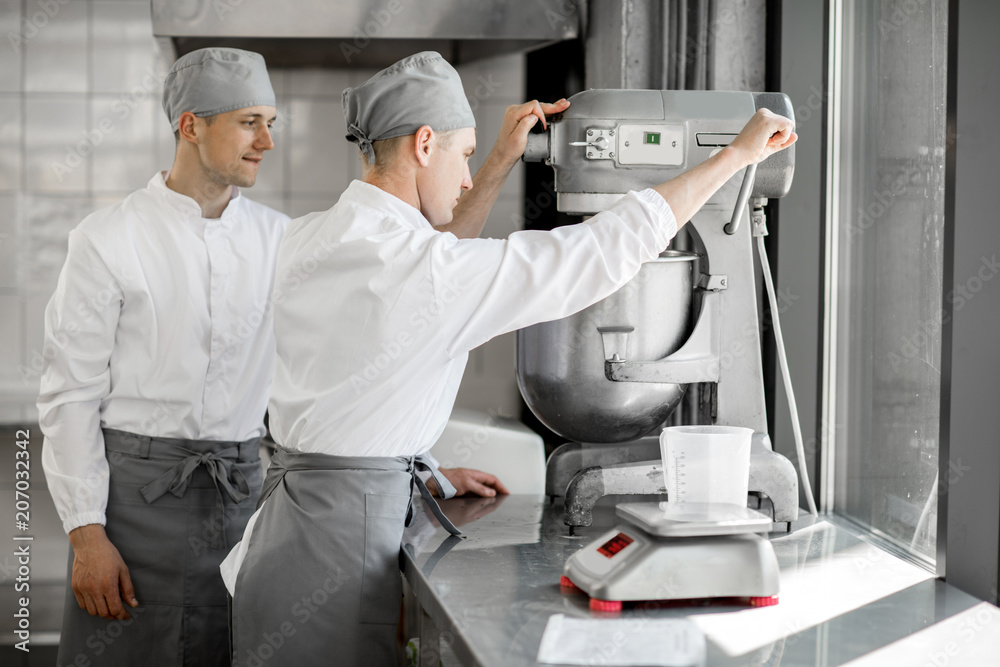 Confectioners working with kneader machine at the bakery manufacturing Confectioners working with kneader machine at the bakery manufacturing