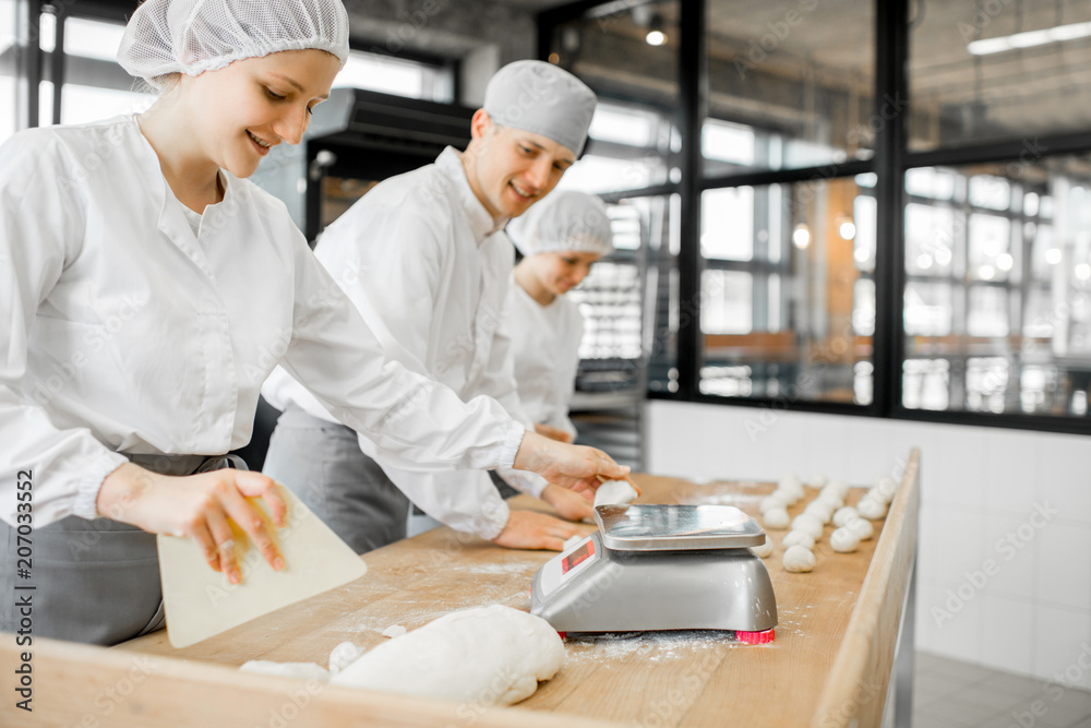 Three bakers having fun forming dough for baking standing together at the modern manufacturing Three bakers having fun forming dough for baking standing together at the modern manufacturing