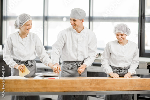 Three bakers having fun forming dough for baking standing together at the modern manufacturing