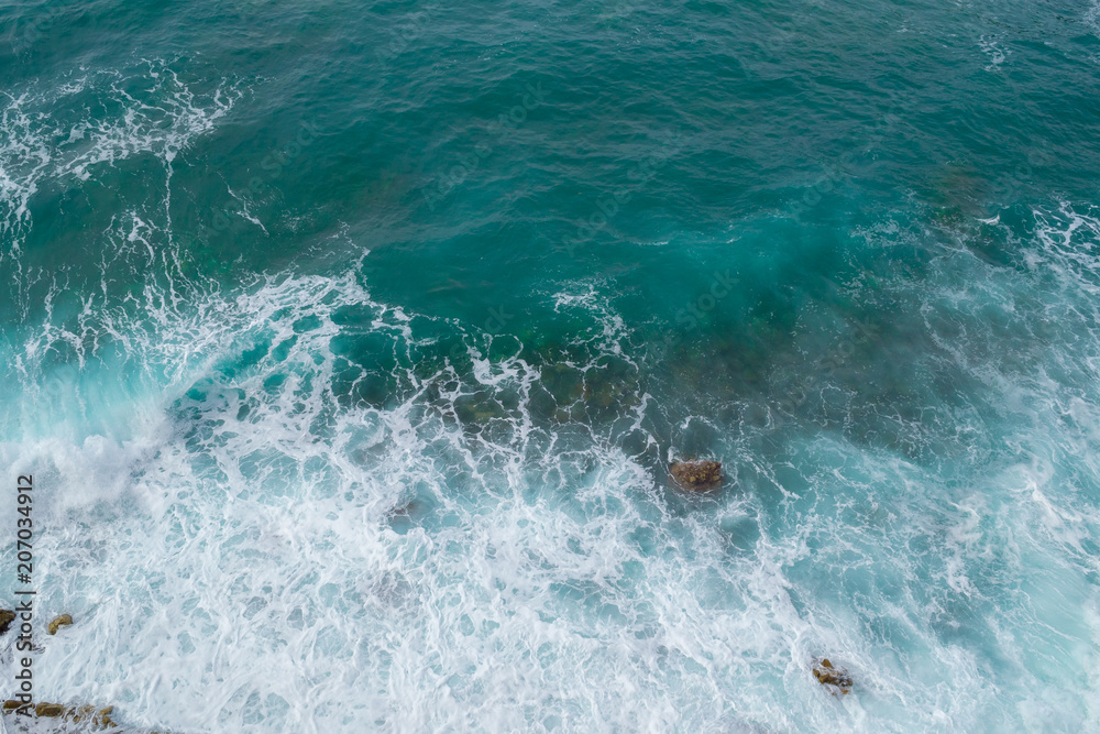 Fototapeta premium Big waves breaking on the shore. Waves and white foam. Coastal stones. View from above. The marine background is green