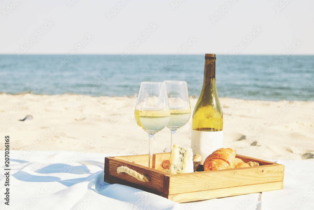Romantic dinner at the beach concept. Expensive bottle of white wine, blank label, two glasses, french croissants, blue brie cheese on wooden tray. Ocean, sea view. Close up, background, copy space. Romantic dinner at the beach concept. Expensive bottle of white wine, blank label, two glasses, french croissants, blue brie cheese on wooden tray. Ocean, sea view. Close up, background, copy space.