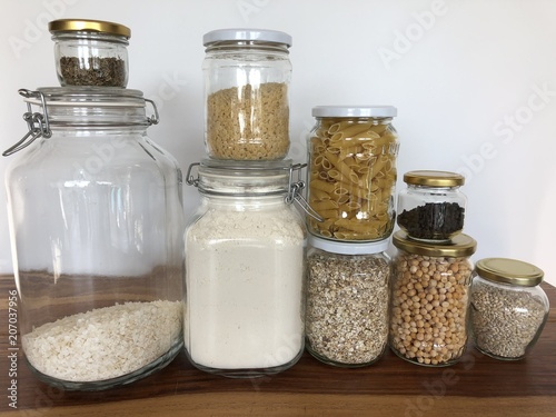 Healthy cereals and fruits in glass jars and reusable bags with fresh basil on wooden background in daylight
