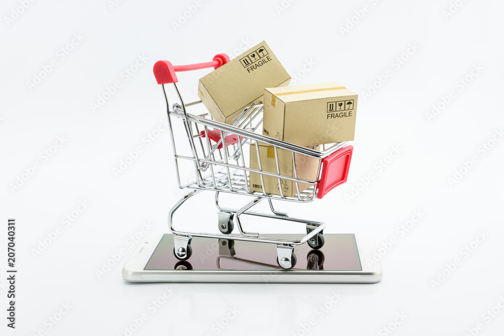 Online shopping and ecommerce via internet concept : Boxes in a shopping cart or metal trolley on a white mobile smartphone . Consumer always buy or shop goods and things from online retail stores .