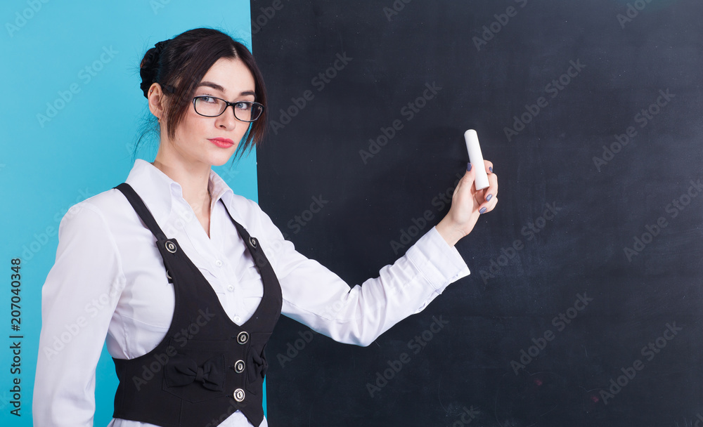 Teacher writing with white chalk on empty blackboard in classroom Teacher writing with white chalk on empty blackboard in classroom