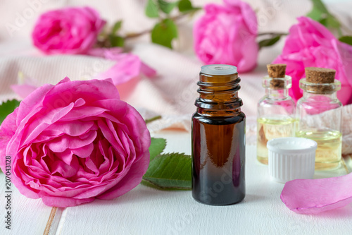 A bottle of essential oil with fresh rose flowers