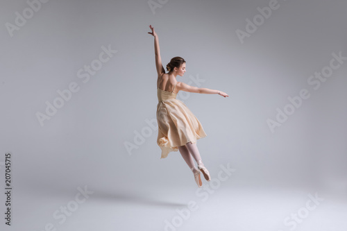 Fototapeta Naklejka Na Ścianę i Meble -  Express yourself! Beautiful tender female ballet dancer with flowing beige fabric dress dancing with grace in the isolated studio.