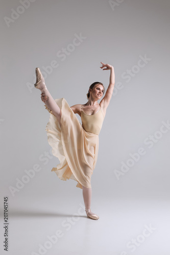 Making a dance! Graceful attractive charming young ballerina in beige outfit posing on toes on the studio background.