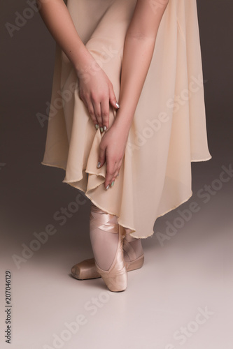 Writing with your feet! Graceful delicate ballerina's feet wearing ballet shoes and hands touching them on the isolated beige background.