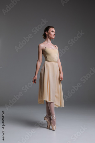 Dance as the narration of a magical story! Side view full length portrait of the young attractive serious professional ballet dancer against the beige background.