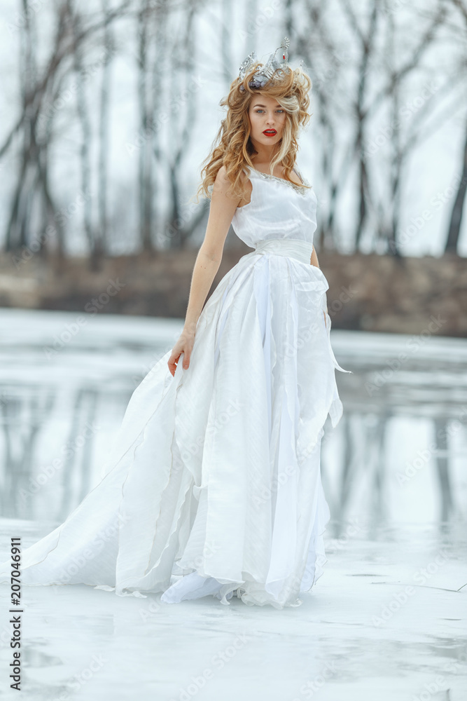 The Snow Queen. Young beautiful girl, blonde, in the image of a snow queen, on ice of a frozen river